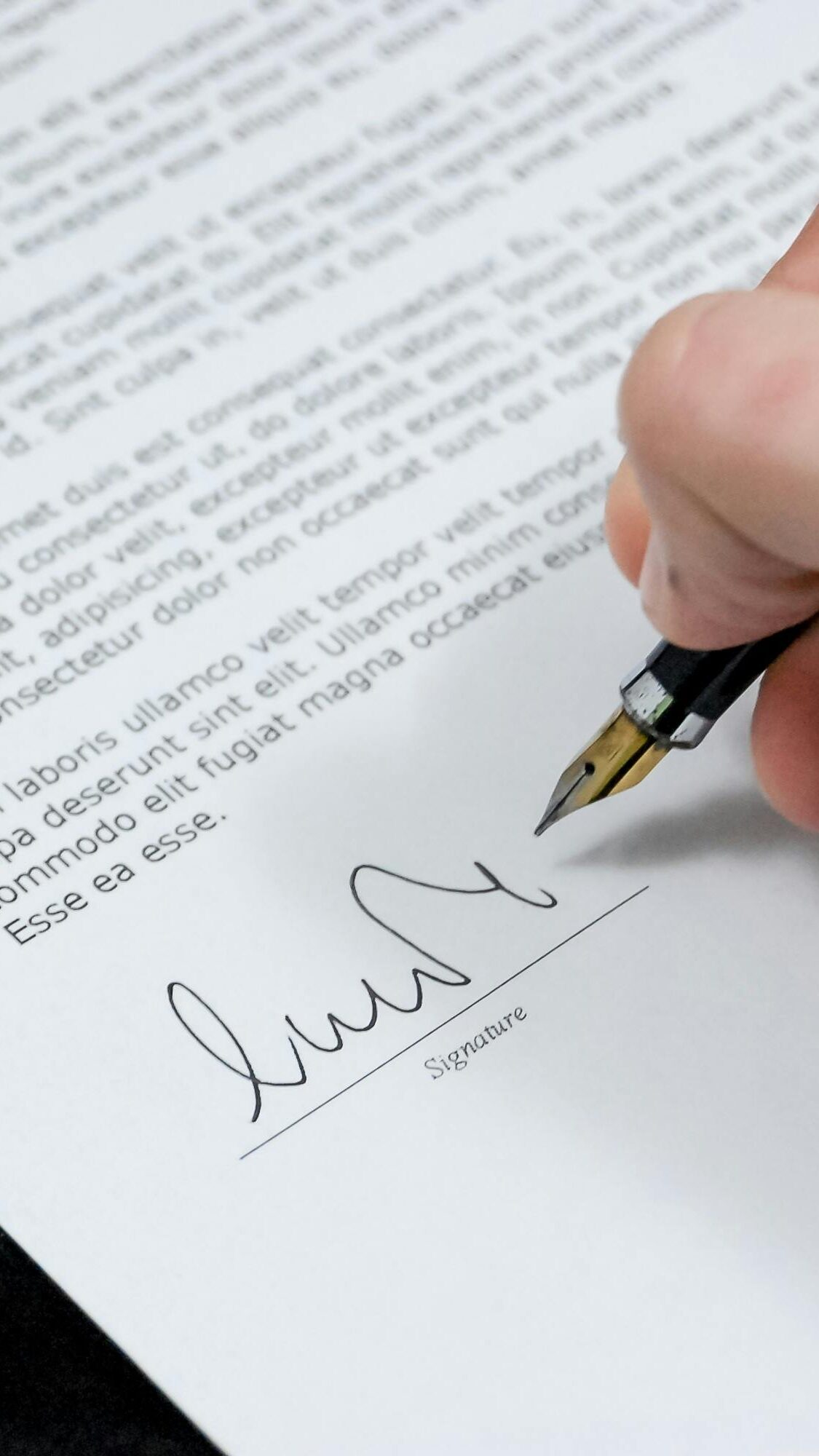 Close-up of a hand signing a formal document with a fountain pen, indicating agreement.