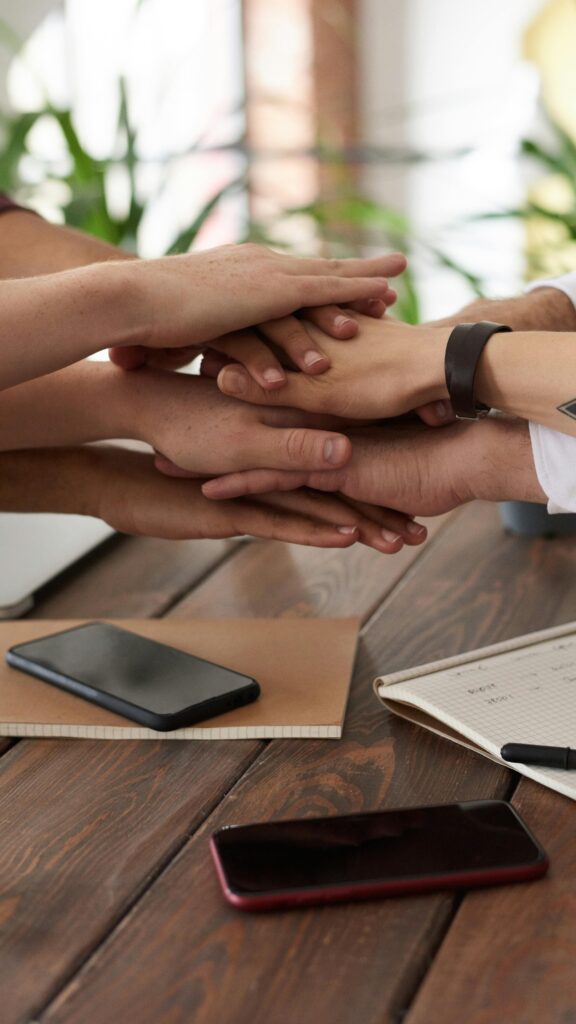 Hands from a diverse team stack on a table symbolizing unity and teamwork in a modern office setting.